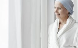 Smiling woman with cancer looking out the window in bathrobe while in the hospital